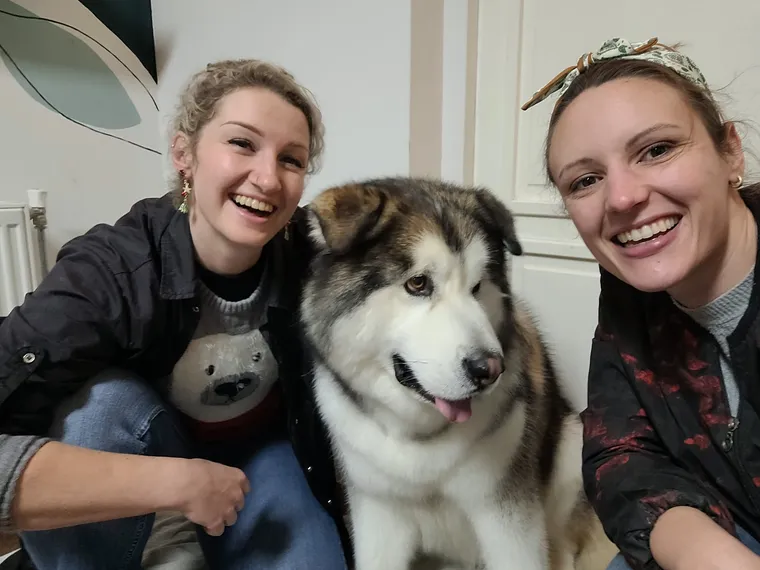 Stagiair Delila en Cynthia lachen samen met Odin, een alaska malamute, in de salon