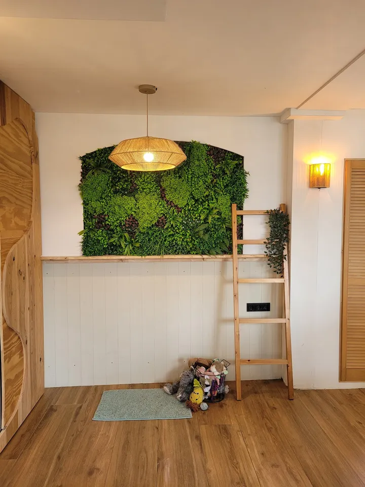 De binnenkomst van de salon, met een groene plantenwand, een houten ladder en een rieten lamp